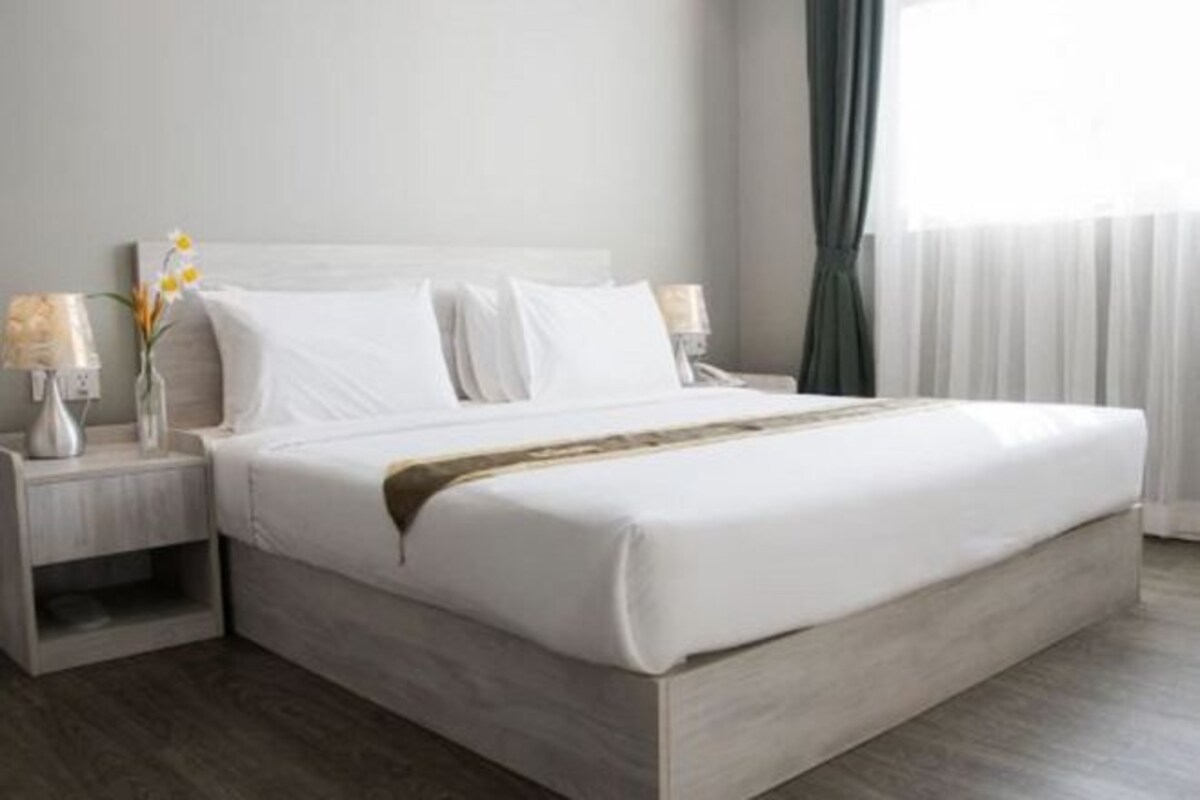 A neatly made bed with white linens, a wooden headboard, and two bedside tables with lamps and a vase of flowers.