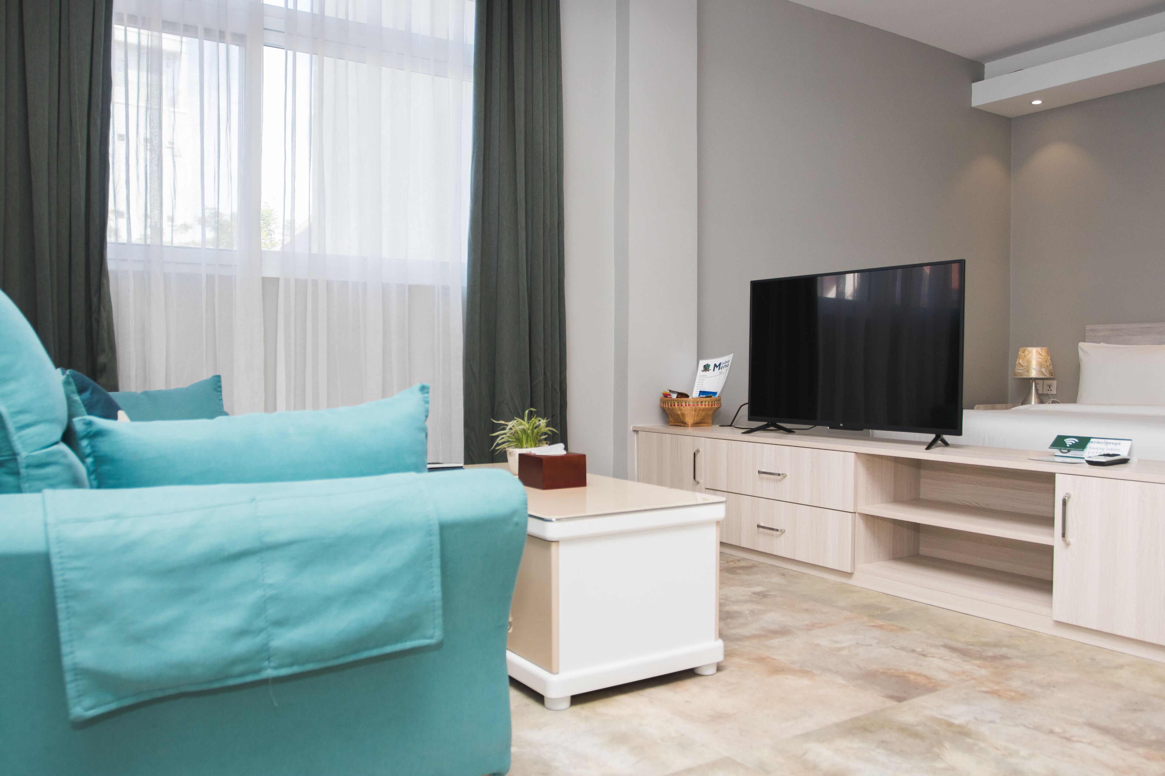 Una sala de estar moderna con un sofá azul turquesa, un televisor de pantalla plana y una mesita de noche con una planta.