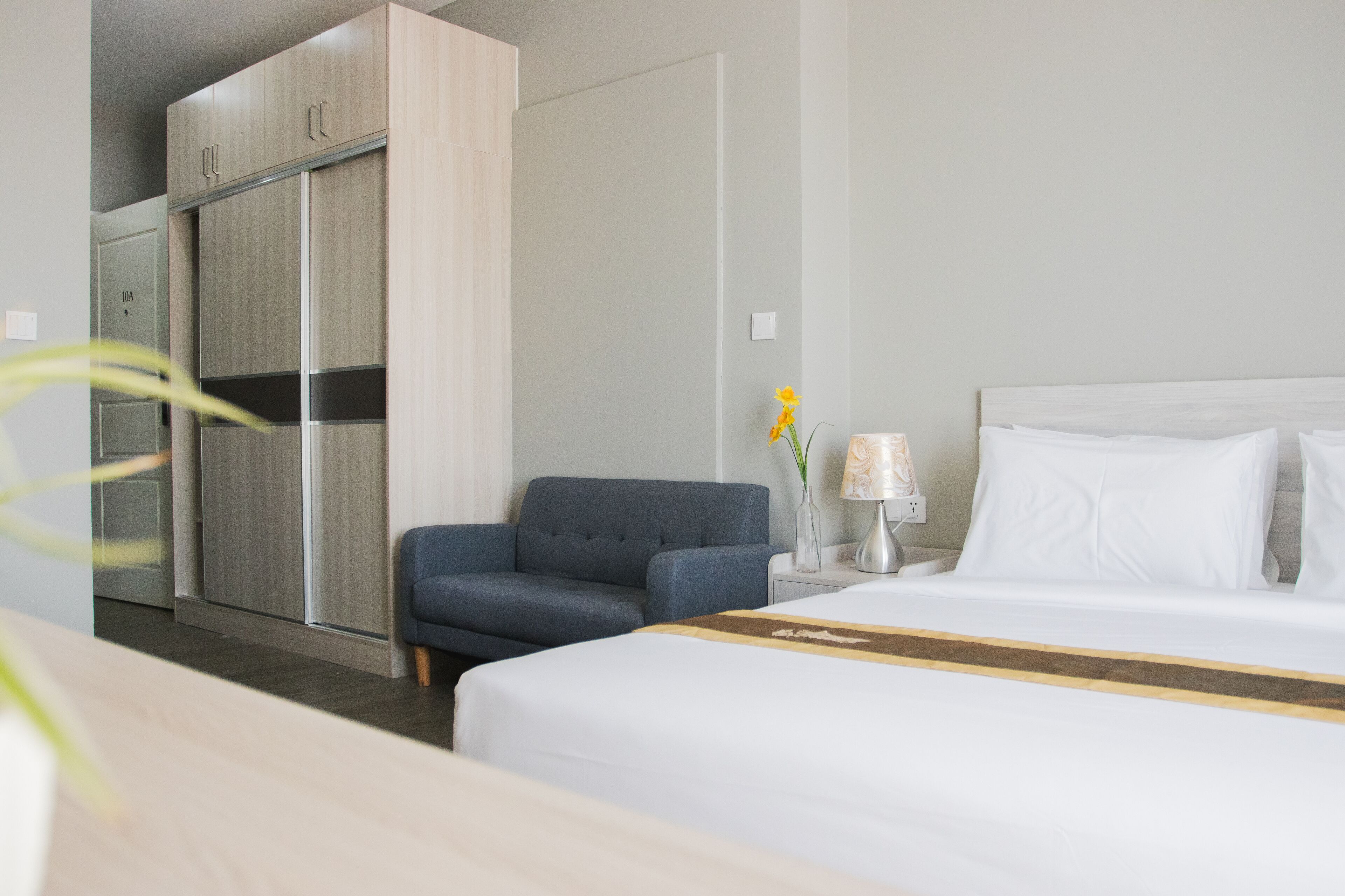 Een hotelkamer met een bed, een bureau, een stoel, een kledingkast en een nachtkastje met een lamp.