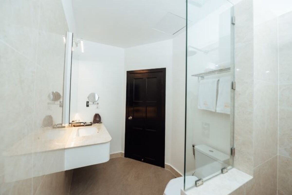 A modern bathroom with a white vanity, a glass shower enclosure, and a dark door.