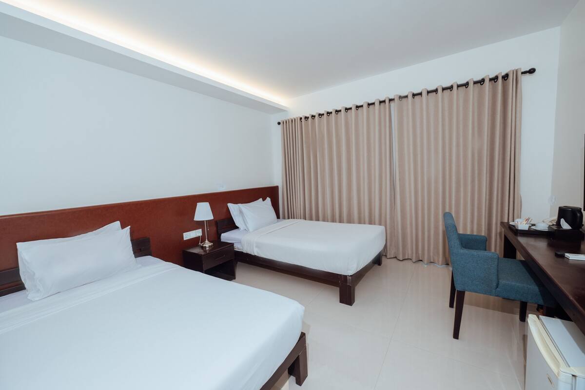 Ein Hotelzimmer mit zwei Betten, einem Schreibtisch, einem Stuhl, einer Lampe und einem Fenster mit Vorhängen.