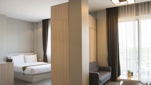 A modern hotel room with a bed, a sofa, a small table, and a large window with curtains. - Cambodian Country Club (Phnom Penh)