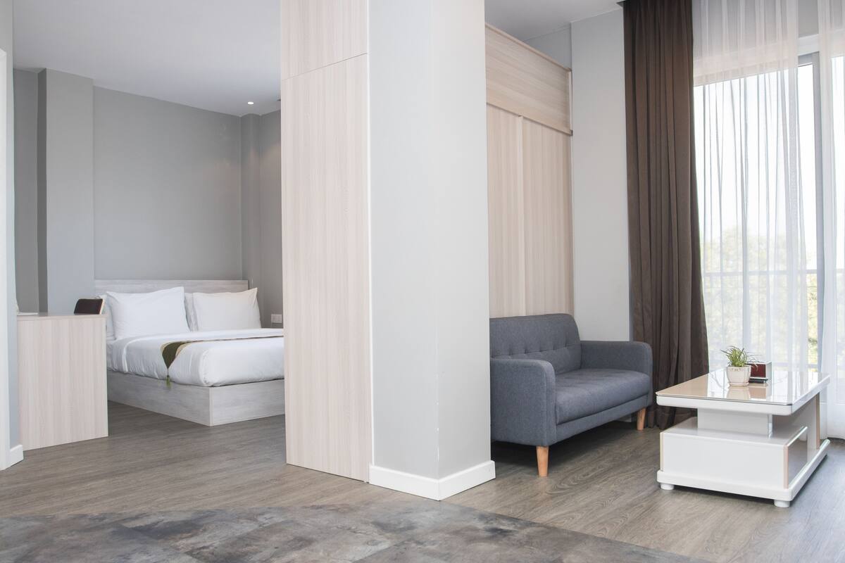 Ein modernes Hotelzimmer mit einem Bett, einem grauen Sofa, einem weißen Couchtisch und einem großen Fenster mit Vorhängen.