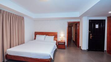 A hotel room with a wooden bed, a bedside table with a lamp, and a door leading to another room.