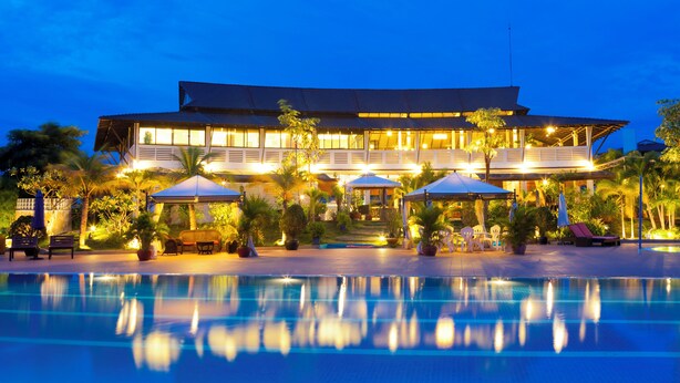 A large hotel with a swimming pool in the foreground, multiple umbrellas, and a well-lit outdoor area with palm trees. - Cambodian Country Club (Phnom Penh)