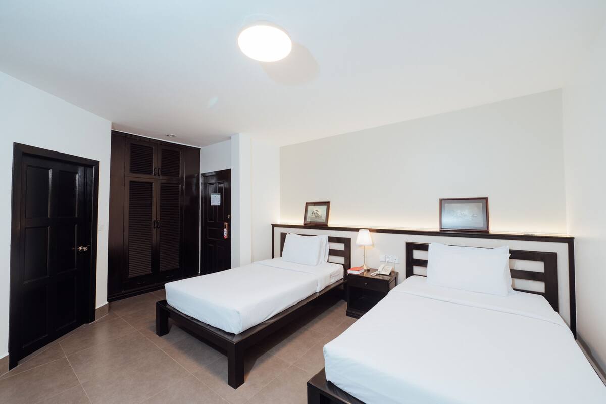Ein Hotelzimmer mit zwei Betten, einem Kleiderschrank und einem Nachttisch mit Lampe.