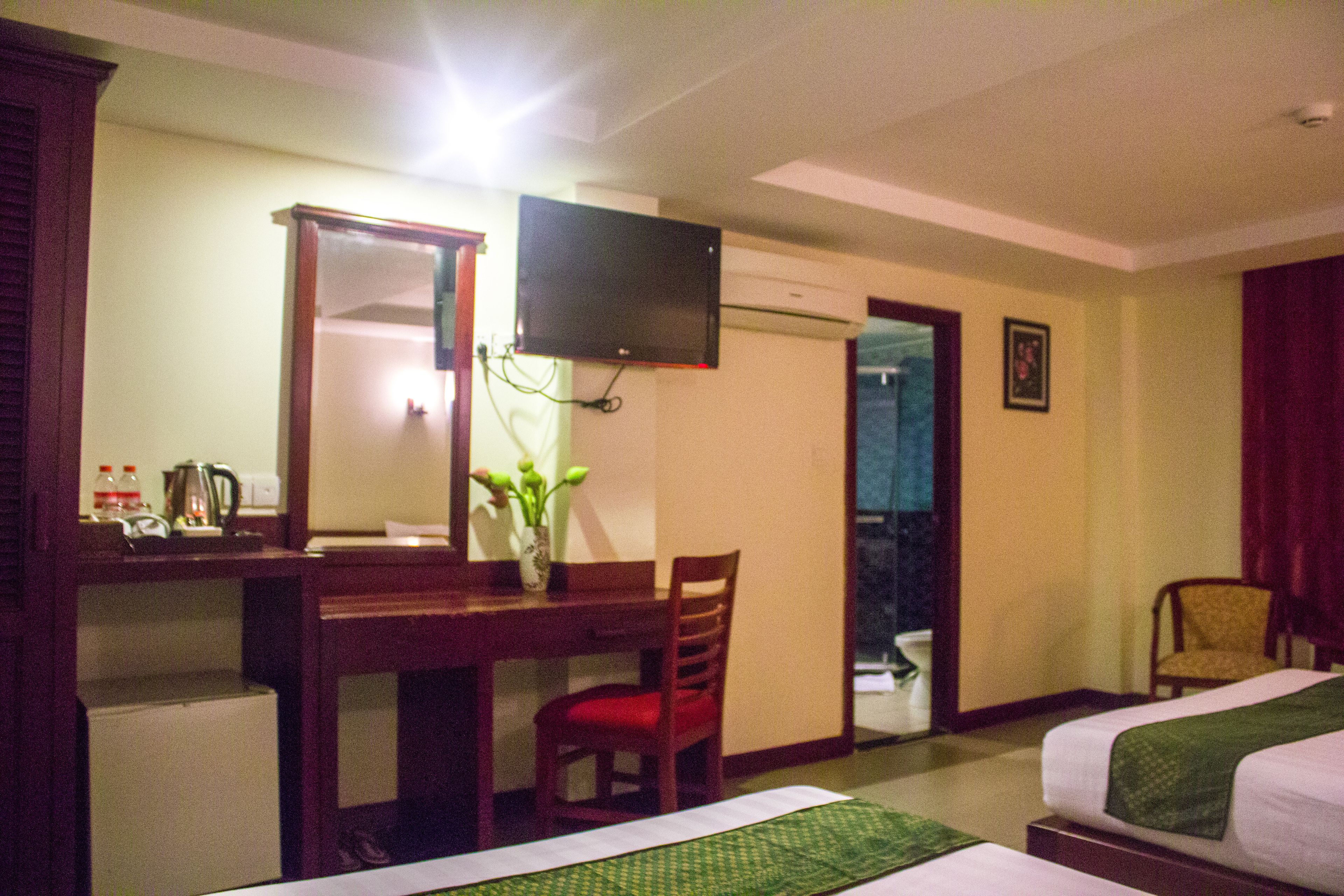 Une chambre d’hôtel comprenant un lit, un bureau avec une chaise, un téléviseur fixé au mur et une petite table sur laquelle est posé un vase de fleurs.