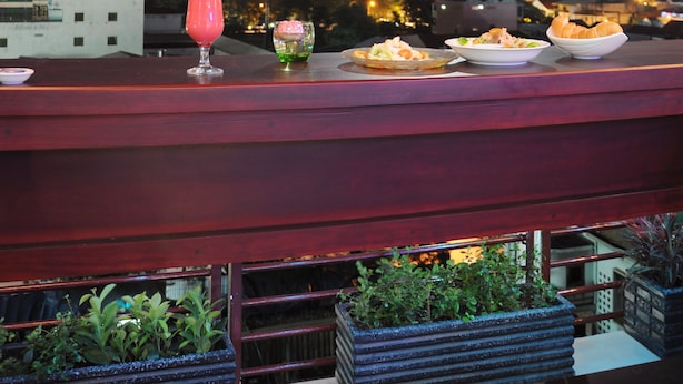 A rooftop bar with a cityscape view, a drink, and a plate of food. - V N E Hotel (Phnom Penh)
