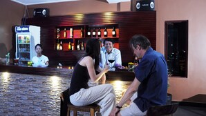 A bar area with a bartender, a seated couple, and a woman in a white shirt behind the bar. - V N E Hotel (Phnom Penh)