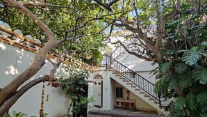 Une cour intérieure avec un escalier menant à un bâtiment blanc, entouré de verdure et de plantes en pot.