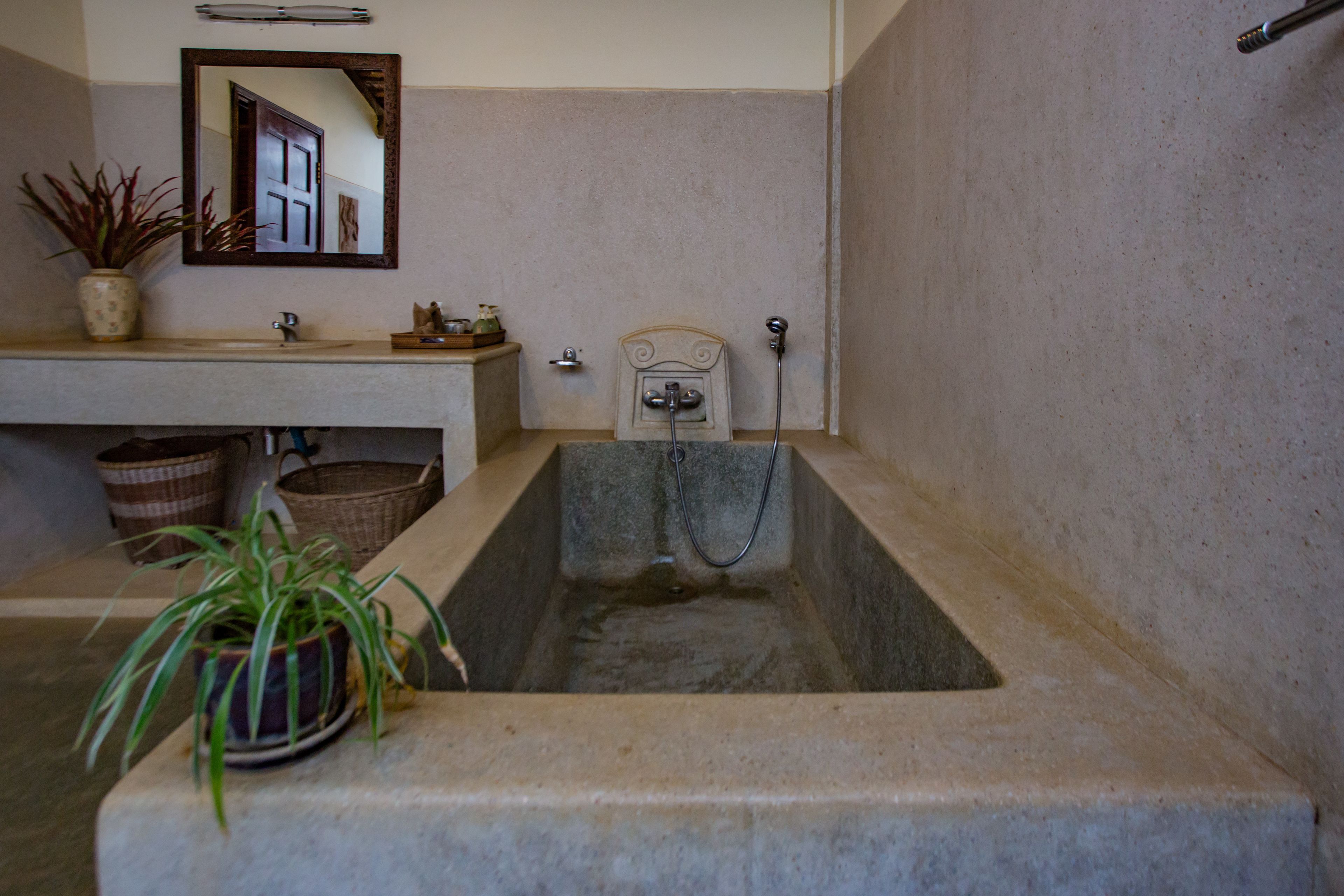 A bathroom with a stone sink, a mirror, a potted plant, and a bathtub.