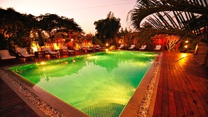 Una piscina rectangular con borde de azulejos, rodeada por una terraza de madera y sillas de descanso.