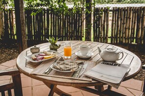 A round wooden table with a newspaper, a teapot, a cup, a glass of orange juice, and a plate of fruit.