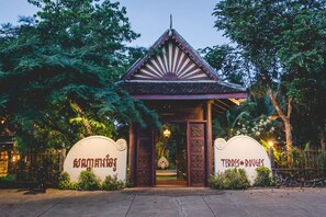 A traditional Thai gate with intricate carvings and a pointed roof, surrounded by lush greenery.
