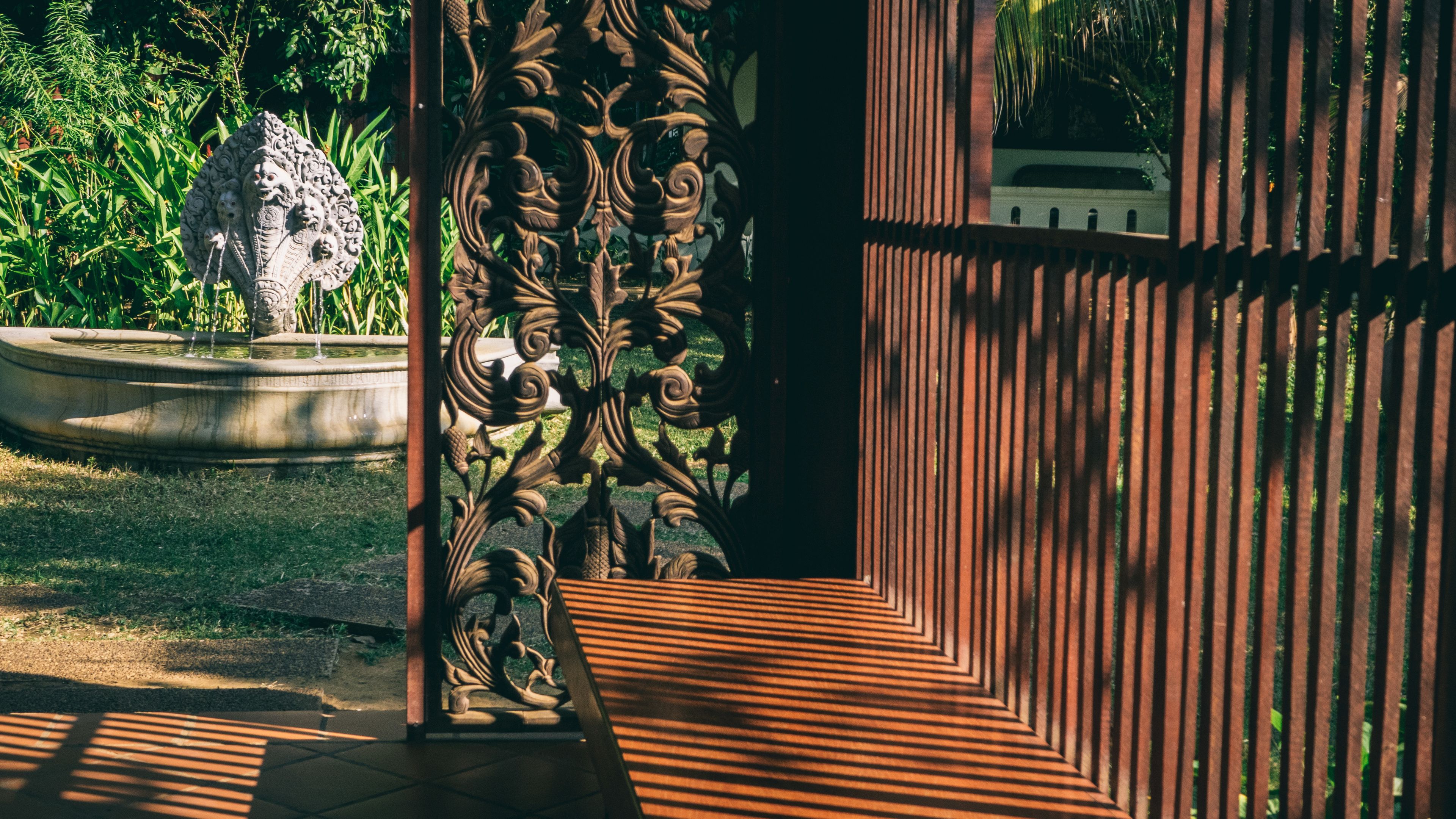 Um jardim com uma fonte, um portão de metal ornamental e um caminho.