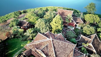 A traditional village with thatched-roof houses surrounded by lush greenery and a calm lake.