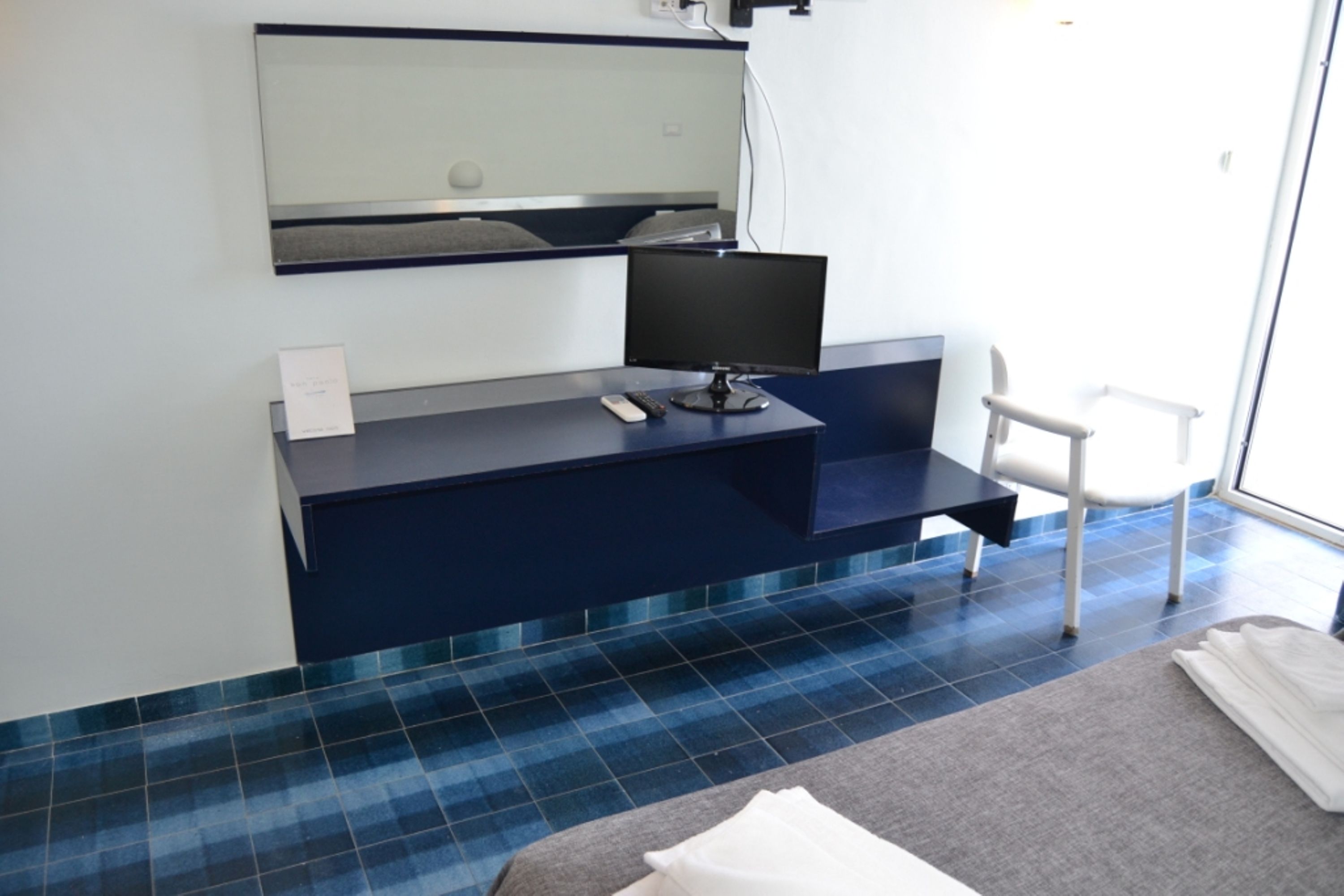 A modern hotel room with a dark blue desk, a flat-screen TV, a chair, and a large window.