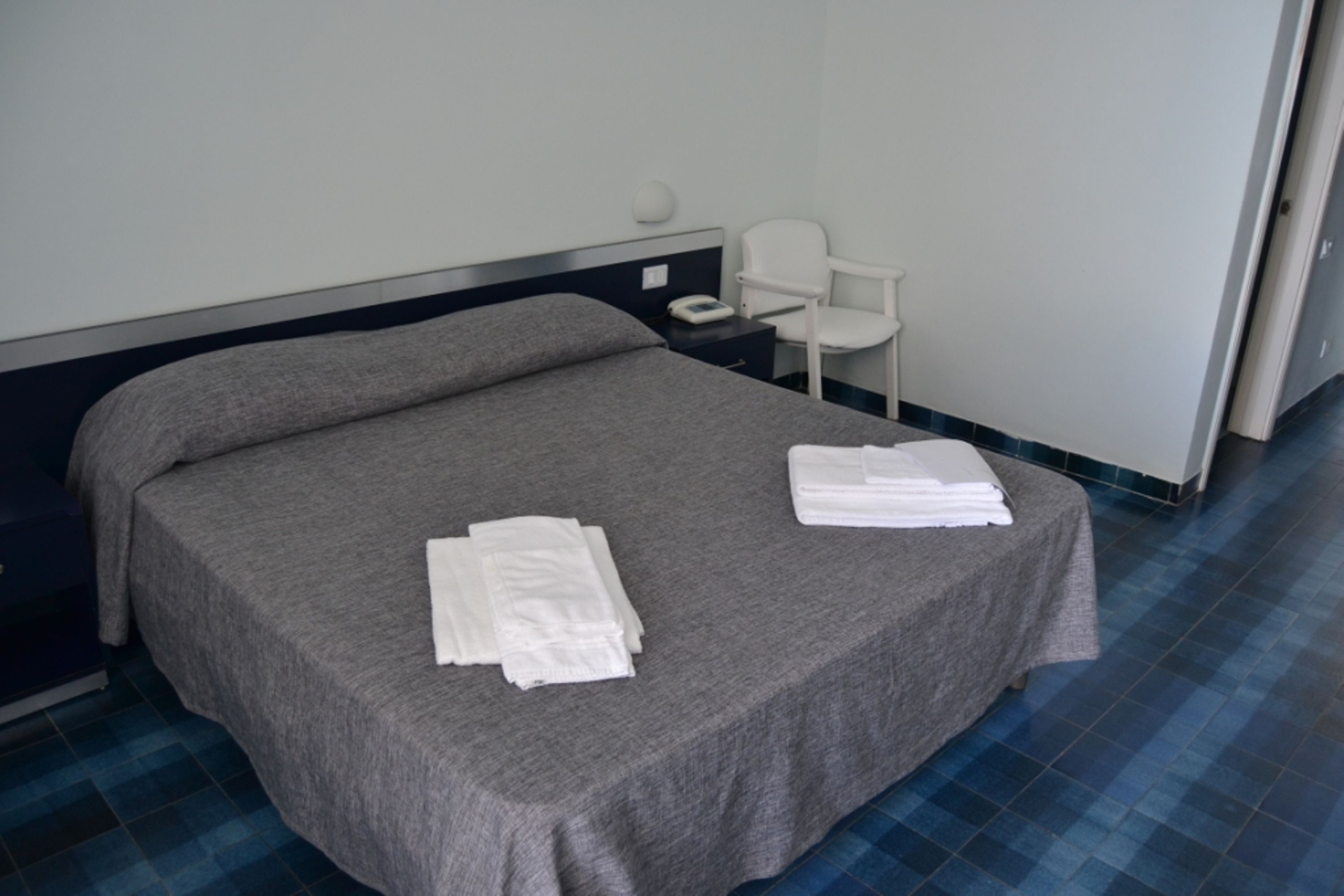 Une chambre d’hôtel avec un lit simple, une chaise et une table de chevet équipée d’un téléphone et d’une lampe.