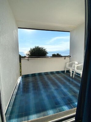 A balcony with blue tiles, white walls, and a view of the sea.