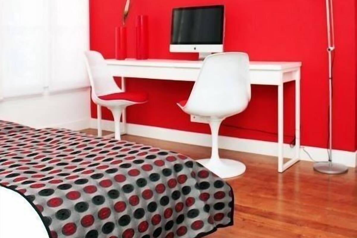 A room with a red wall, white desk, and two white chairs.