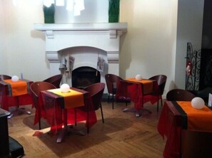 Un comedor con suelo de madera, mesas con manteles naranjas y sillas rojas.