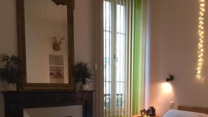 A bedroom with a bed, a desk, two chairs, a mirror, a fireplace, and a window with curtains. - b11 Hôtel (Nice)
