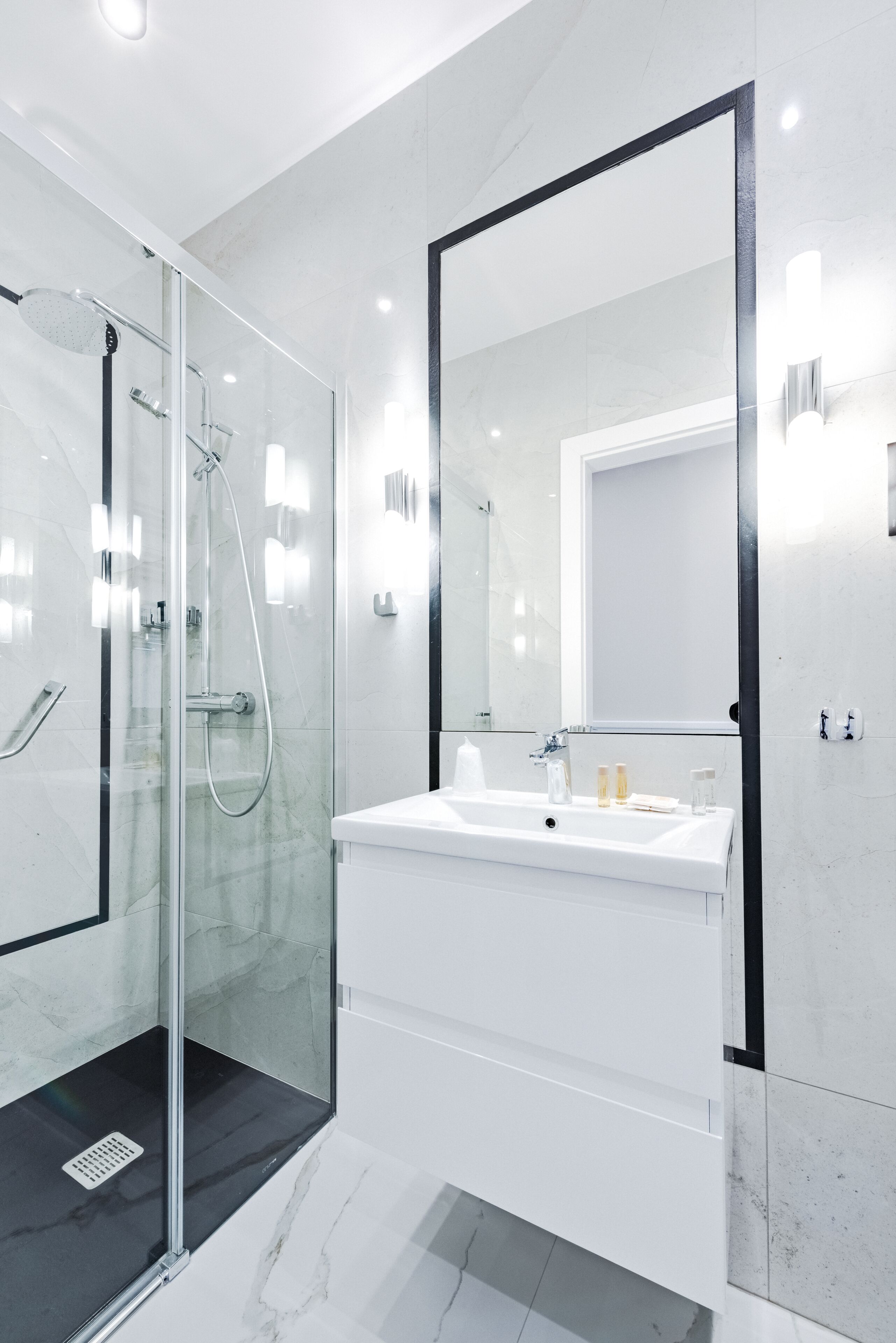Un baño moderno con ducha de vidrio, un lavabo blanco y un espejo grande.