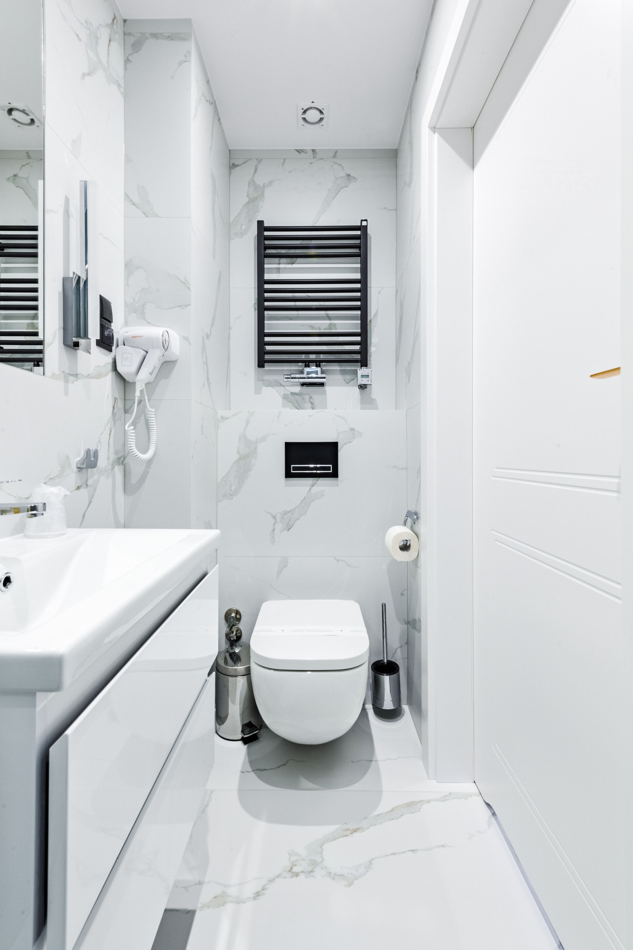 A modern bathroom with a white marble floor, a white toilet, a sink, and a towel rack.