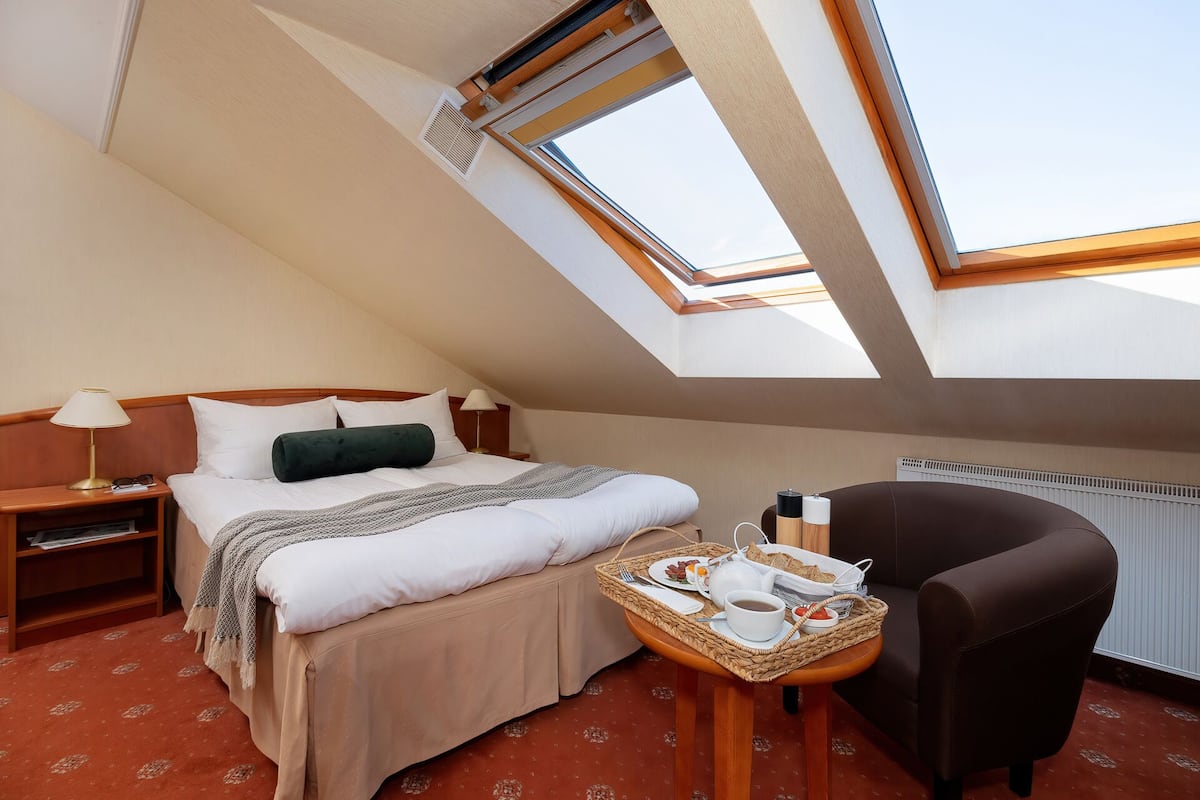 A hotel room with a bed, a chair, a small table with breakfast items, and a skylight.