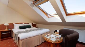 A hotel room with a bed, a chair, a small table with breakfast items, and a skylight.