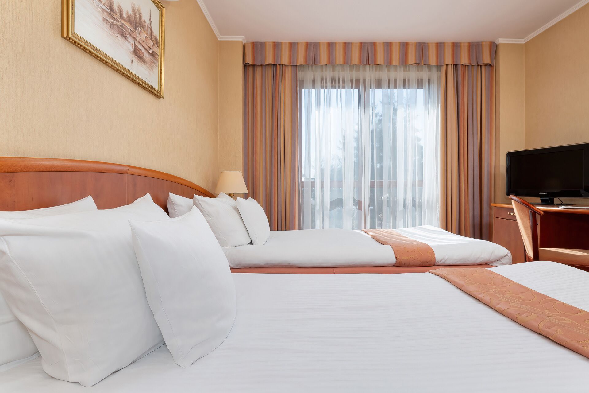A hotel room with a large bed, a television, and a window with curtains.