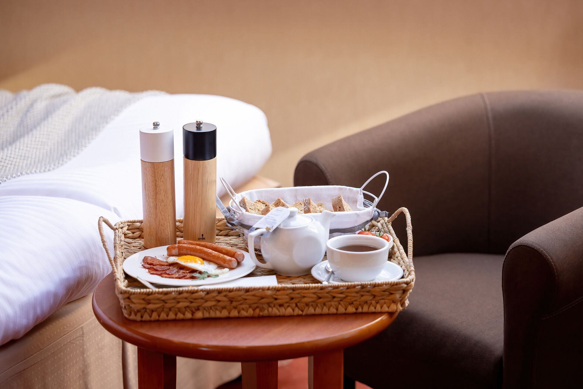 En bakke med morgenmad – æg, pølser, ristet brød, kaffe og te – står på et lille bord ved siden af sengen.