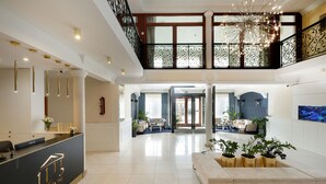 A spacious lobby with a reception desk, a seating area with sofas, a large chandelier, and a view of the outside through a glass door. - Villa Hoff Wellness & SPA Hotel (Rewal)