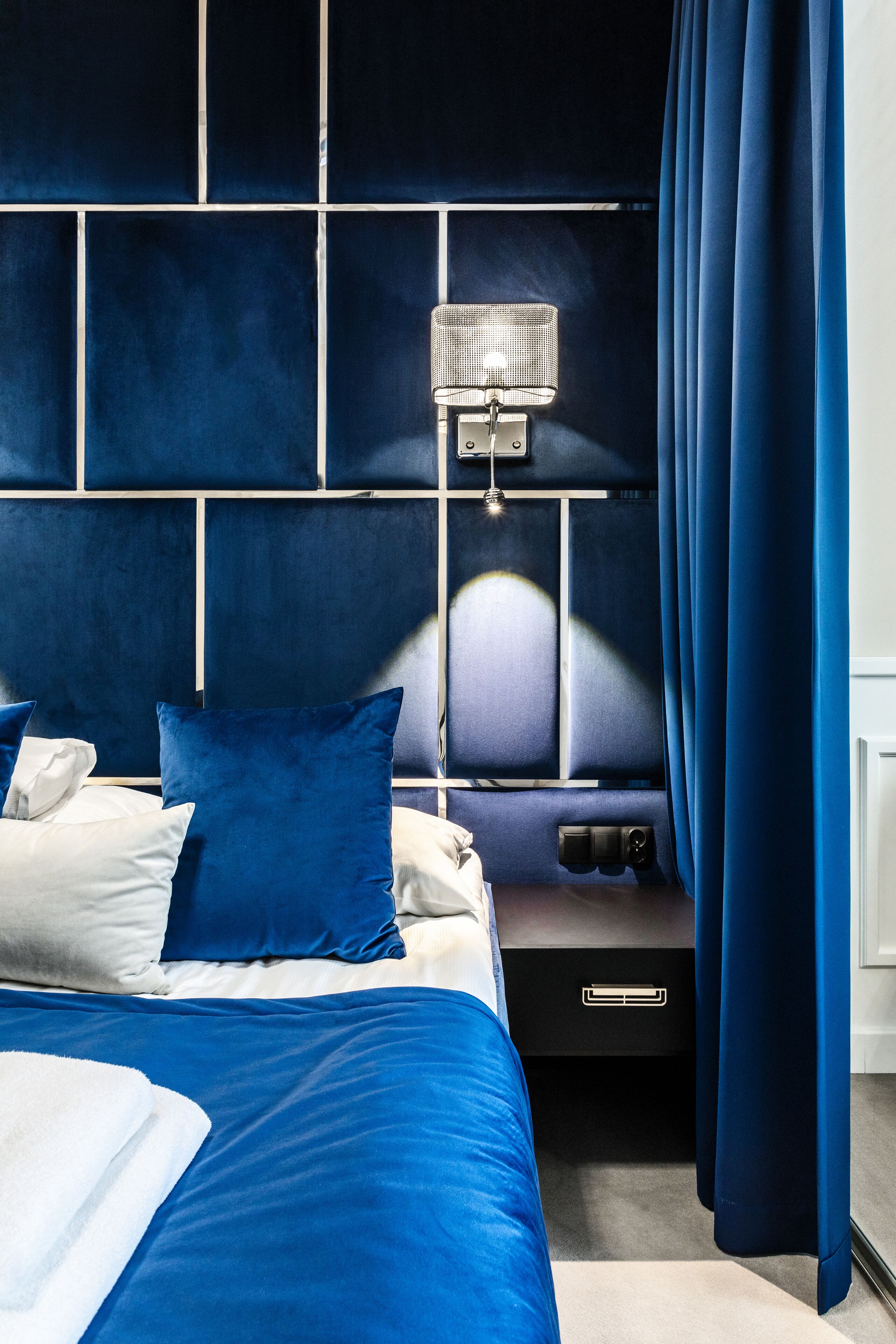 Un dormitorio moderno con una cabecera azul, una mesita de noche con lámpara y ropa de cama azul y blanca.