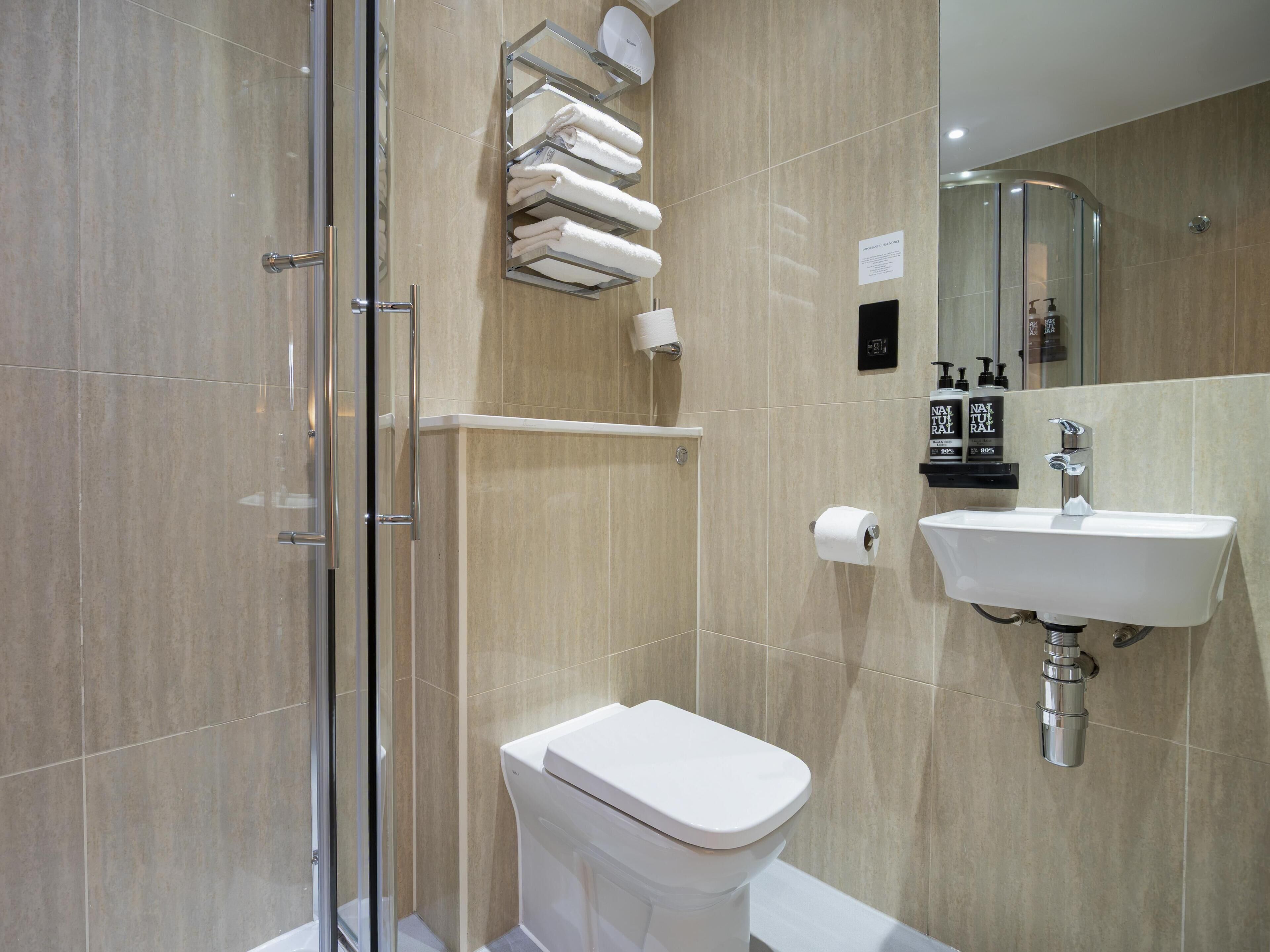 A modern bathroom with a glass shower enclosure, a white toilet, a sink with a mirror, and a towel rack with neatly folded towels.
