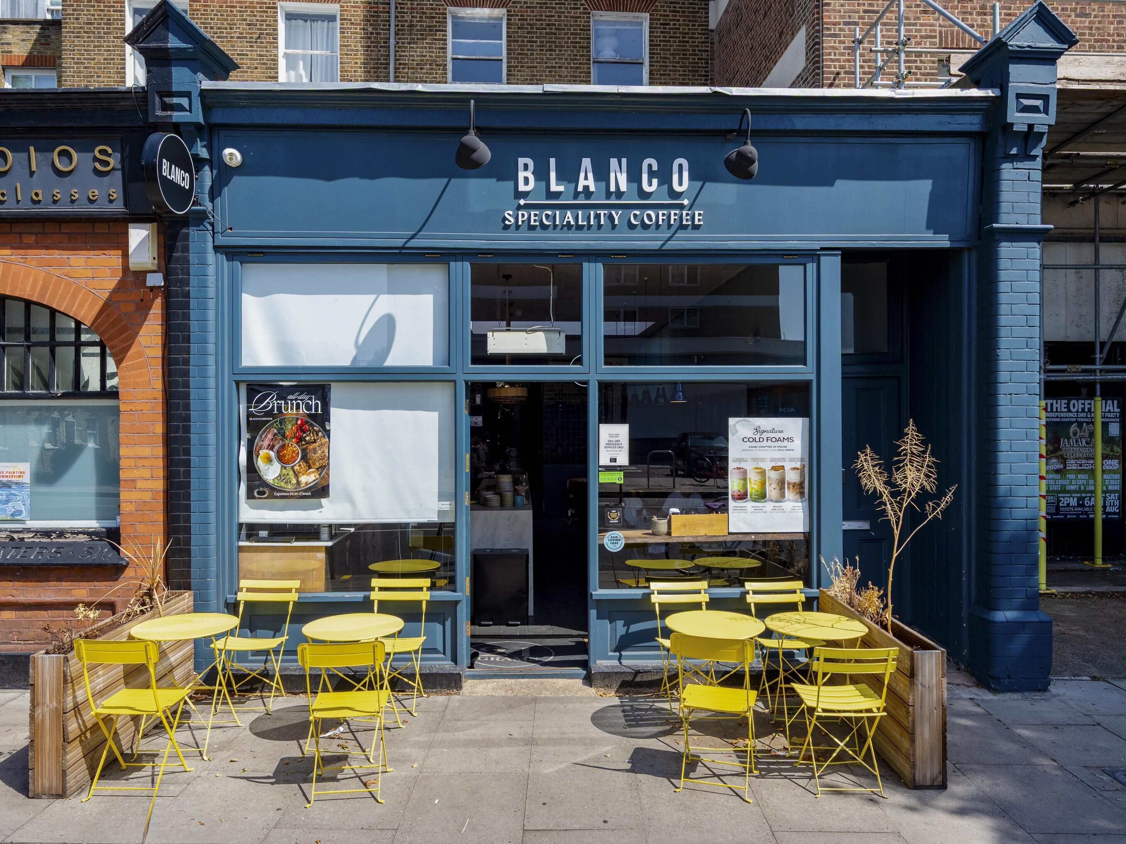 A blue storefront with the name 'BLANCO Specialty Coffee' and outdoor yellow tables and chairs.