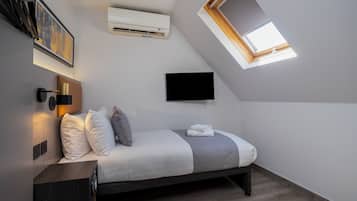 A bedroom with a bed, a mounted TV, an air conditioning unit, a wall-mounted light, and a skylight.