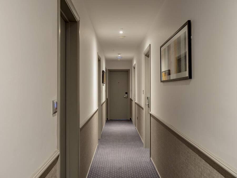 Een hotelgang met een tapijtvloer, deuren en een ingelijste foto aan de muur.
