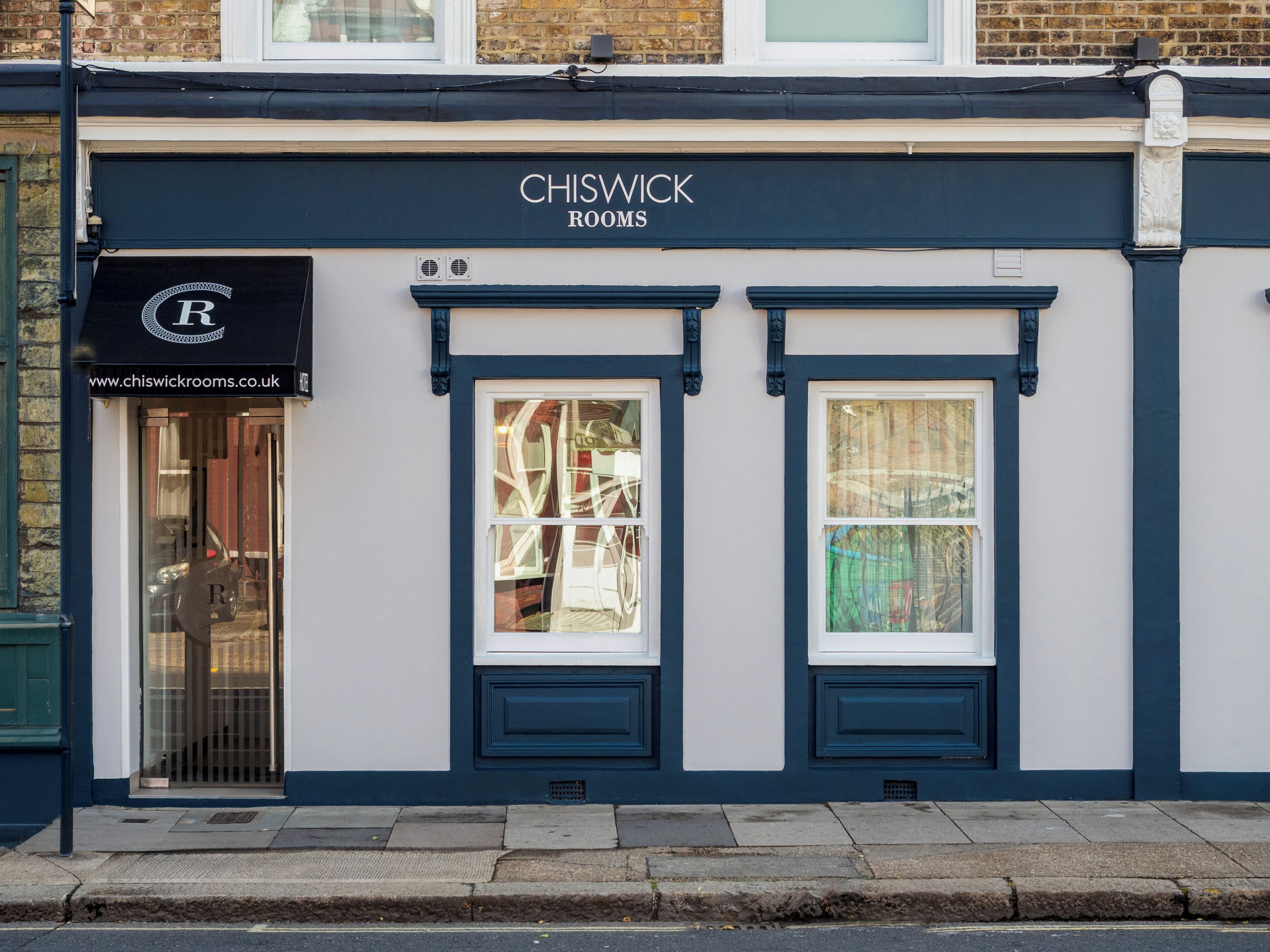 En byggnad med en skylt där det står ”CHISWICK ROOMS” och en webbadress, ”www.chiswickrooms.co.uk”, som syns.