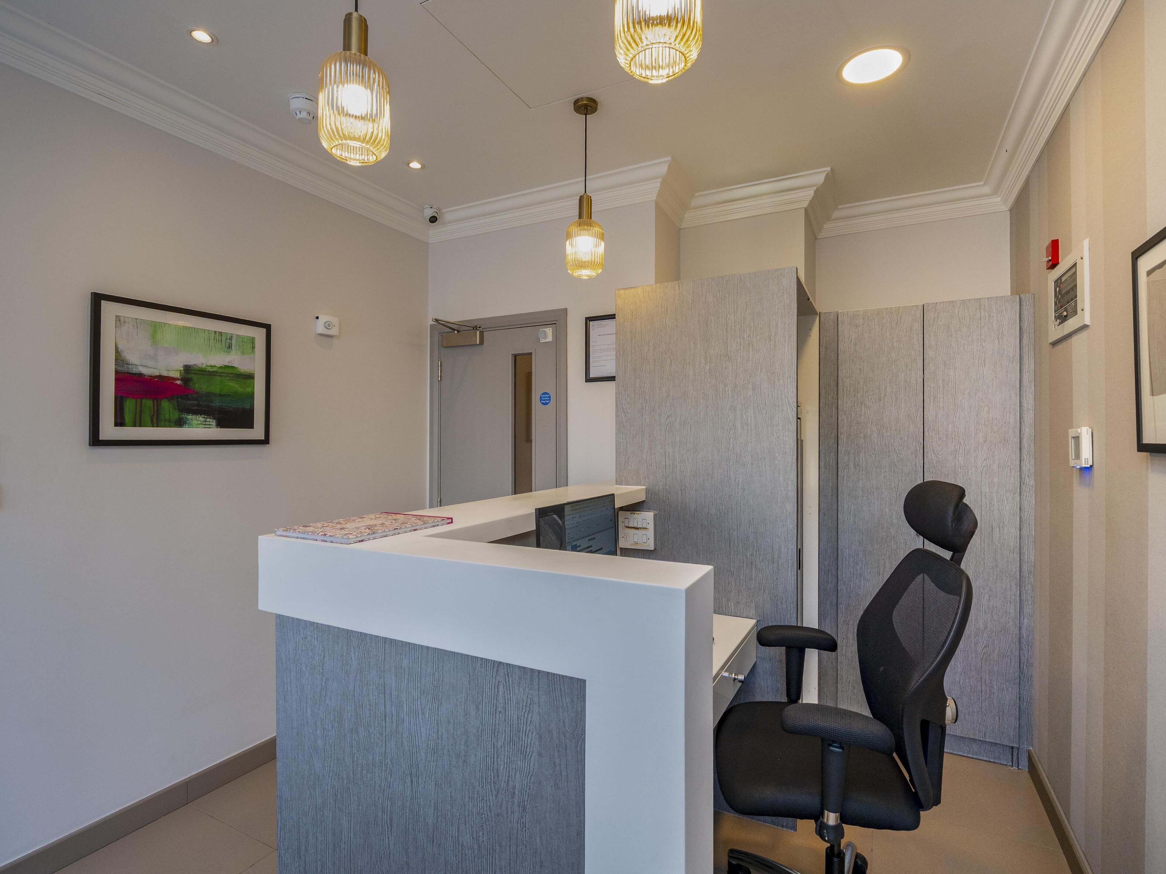 Un'area reception con una scrivania, una sedia da ufficio nera, illuminazione a sospensione e un quadro astratto appeso alla parete.