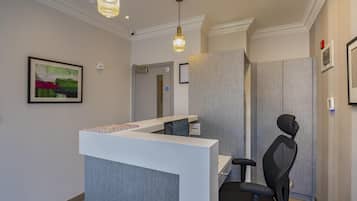 A reception area with a reception desk, a black office chair, pendant lighting, and a framed abstract painting on the wall.