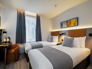 Habitació d'hotel amb dos llits, un escriptori amb una làmpada, una cadira i un quadre a la paret.
