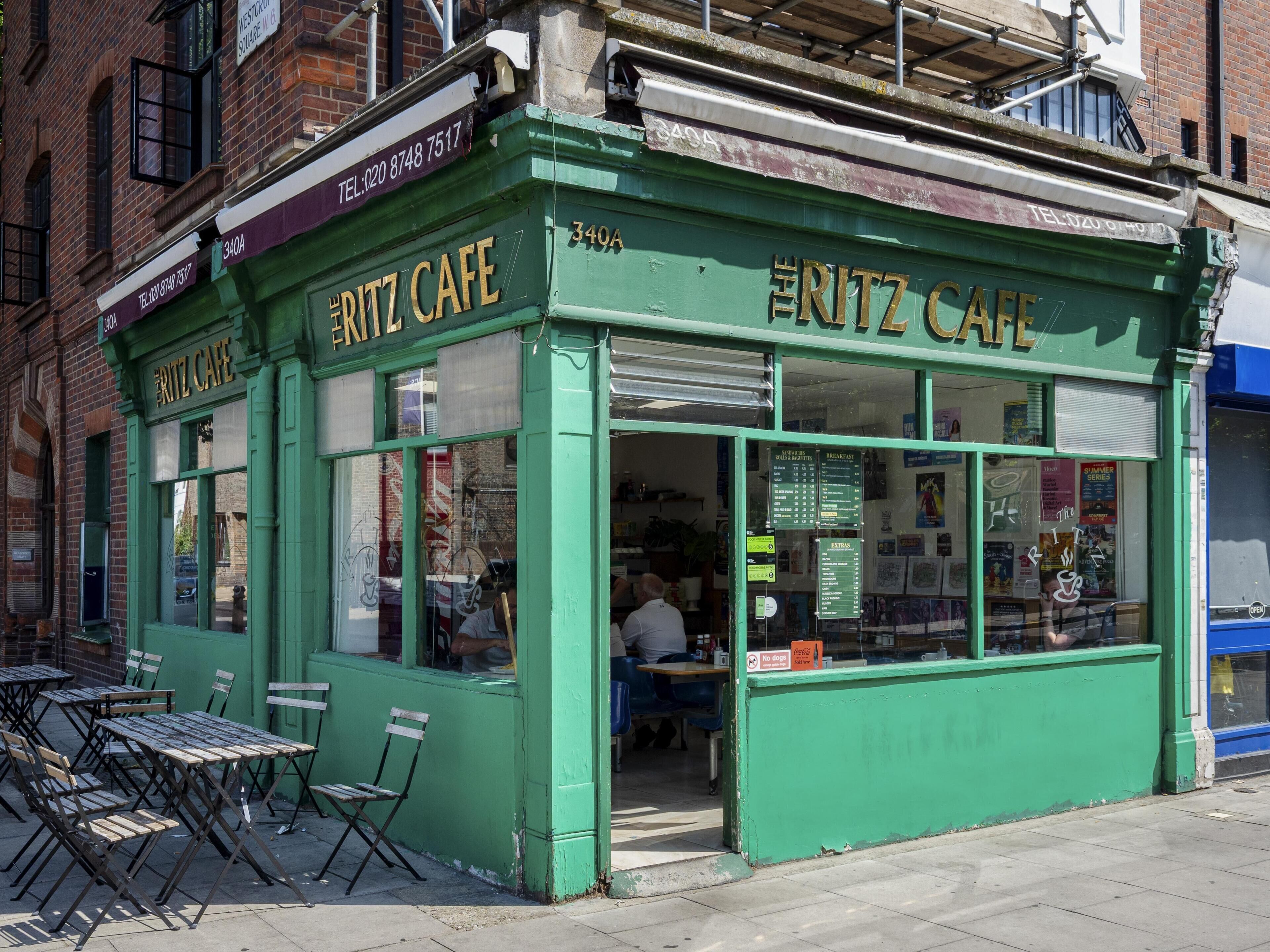 A green exterior of The Ritz Cafe with outdoor seating and a visible menu board.