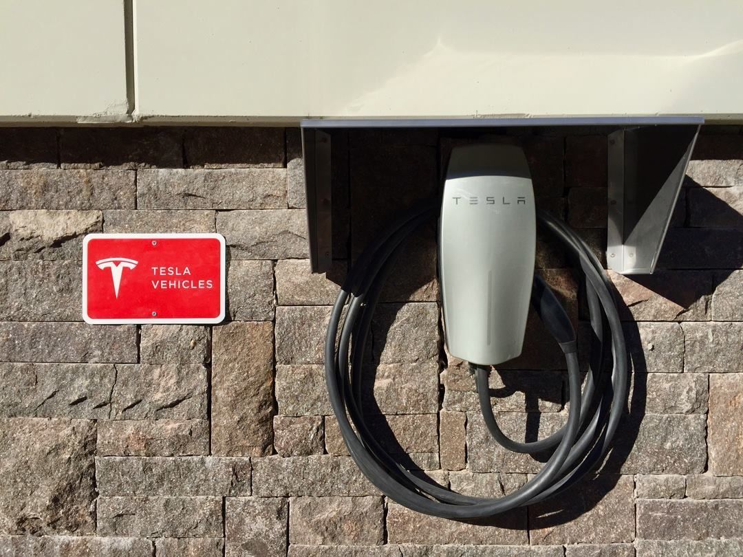 Eine Tesla-Ladestation, an einer Ziegelwand befestigt, mit einem Schild für Tesla-Fahrzeuge.