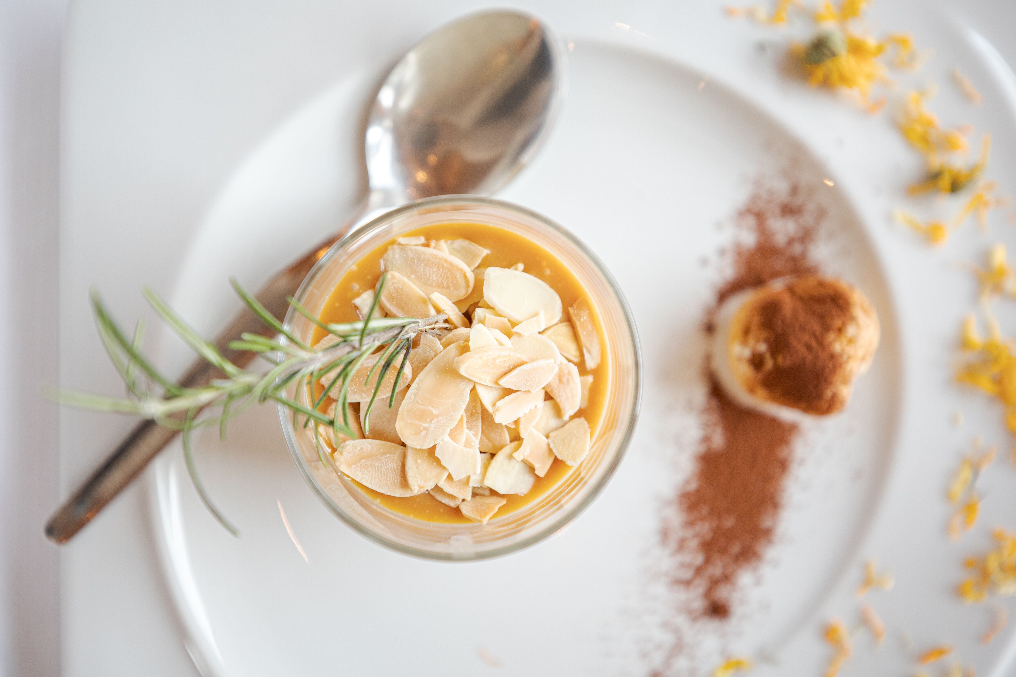 A dessert in a glass bowl on a white plate, garnished with almonds and a sprig of rosemary.