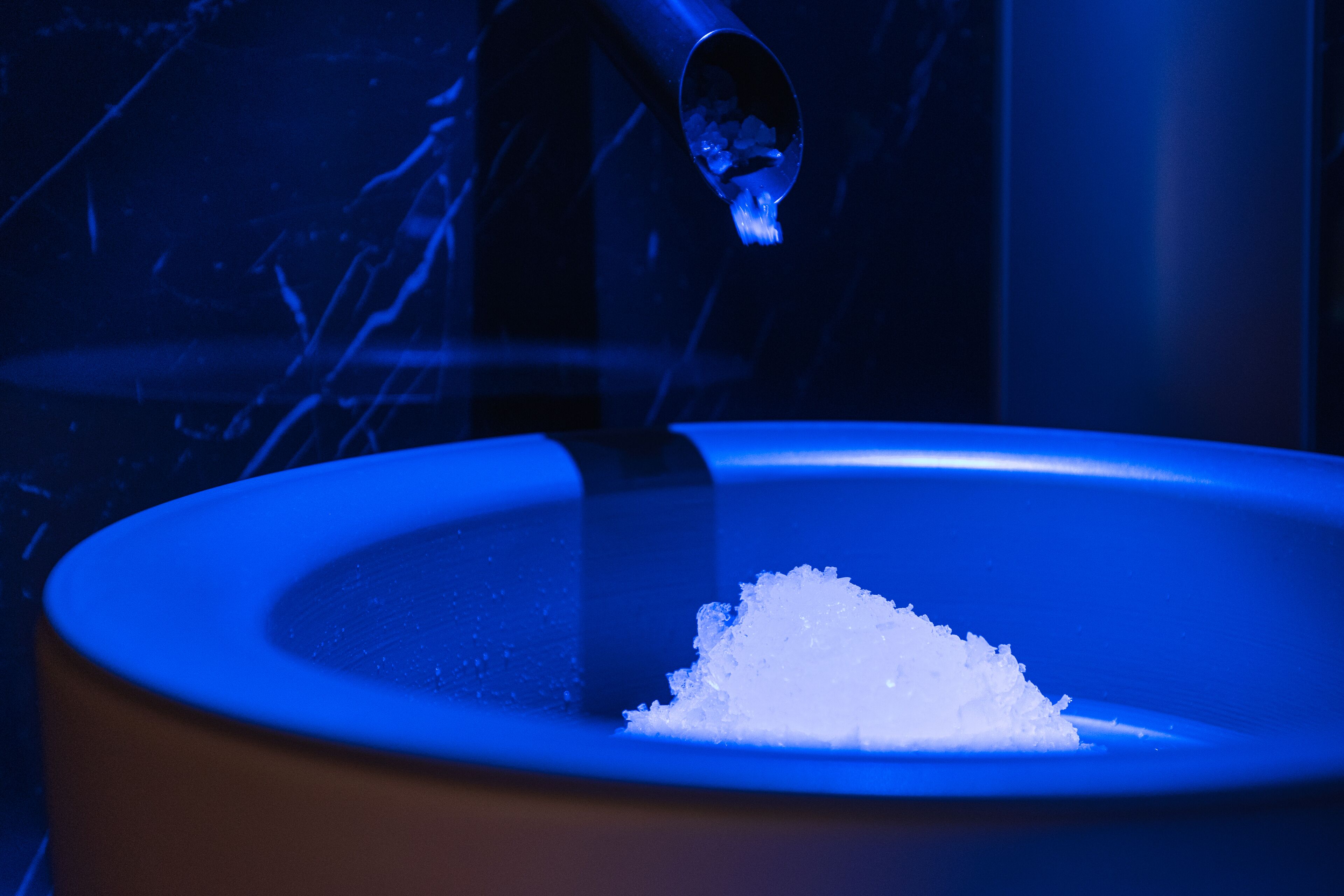 A blue bowl with a scoop pouring white powder into it.