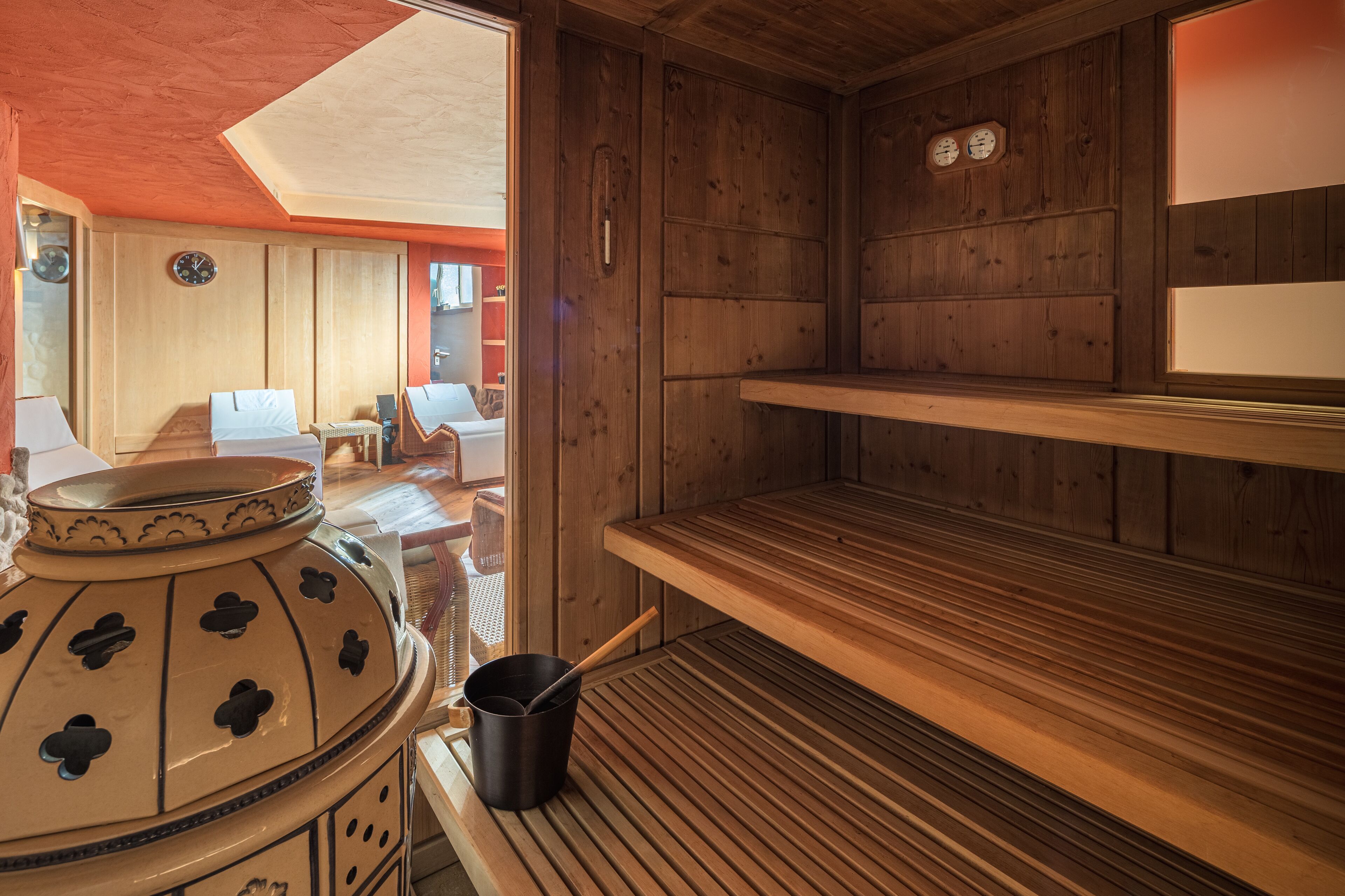 A sauna room with wooden benches, a large ceramic pot, and a wooden shelf.