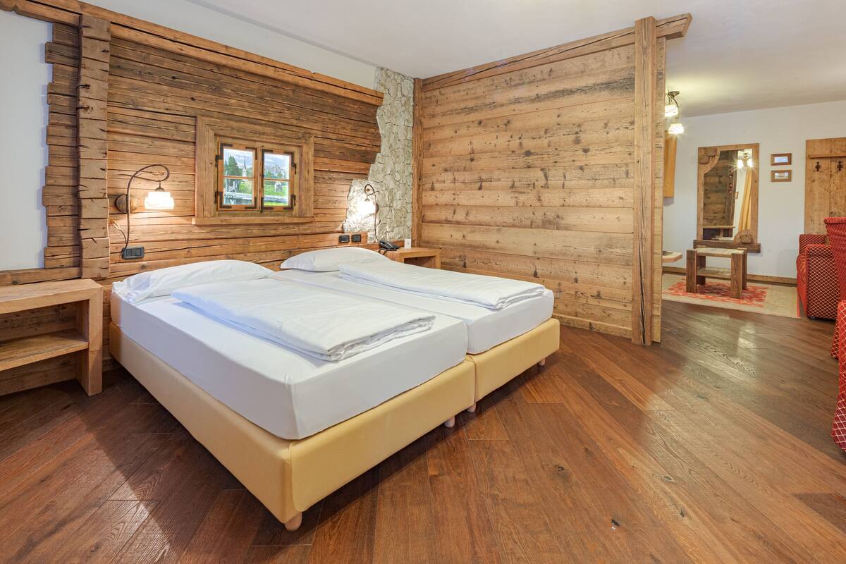 A wooden-paneled room with a double bed, bedside tables, a lamp, and a mirror.