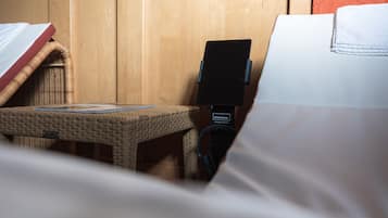 A wicker chair with a smartphone holder, a bed with a white cover, and a wooden wall.