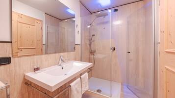A modern bathroom with a large mirror, a white sink, and a glass-enclosed shower.